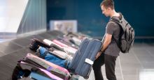 junger Tourist in T-Shirt holt einen Koffer aus der Gepäckausgabe am Flughafen