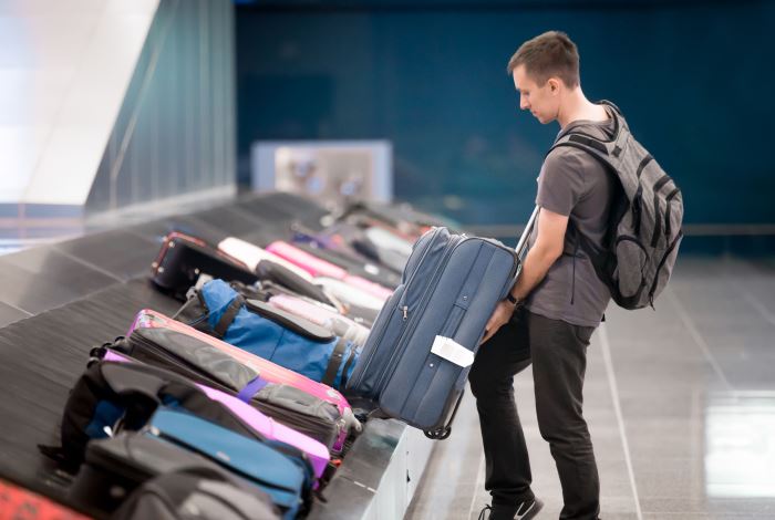 Junger Mann bei der Gepäckausgabe am Laufband am Flughafen entnimmt blauen Koffer