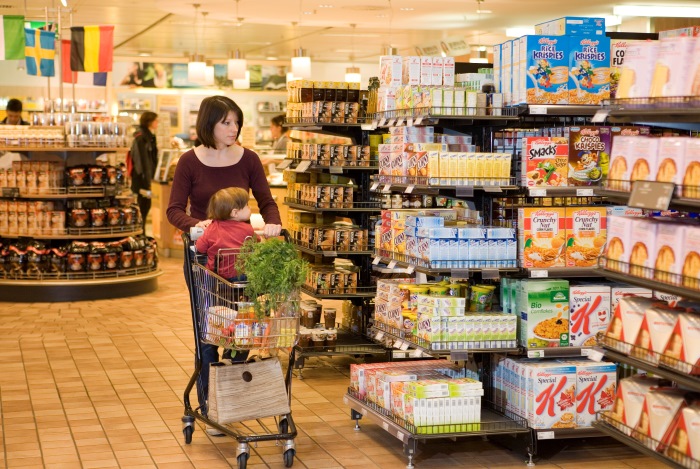 Mutter schiebt Einkaufswagen mit Kleinkind durch Supermarktregale
