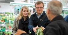 Quadratischer Banner des Aktionsplans Bio aus BW mit SChriftzug und einem jungen Paar beim Einkauft von Gemüse an einem Marktstand