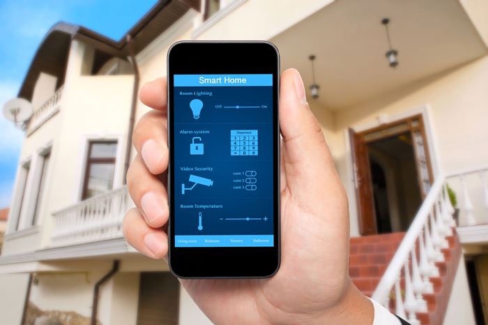 Eine Hand mit Smartphone mit Steuerelementen auf dem Display in Großaufnahme, dahinter ein Hauseingang