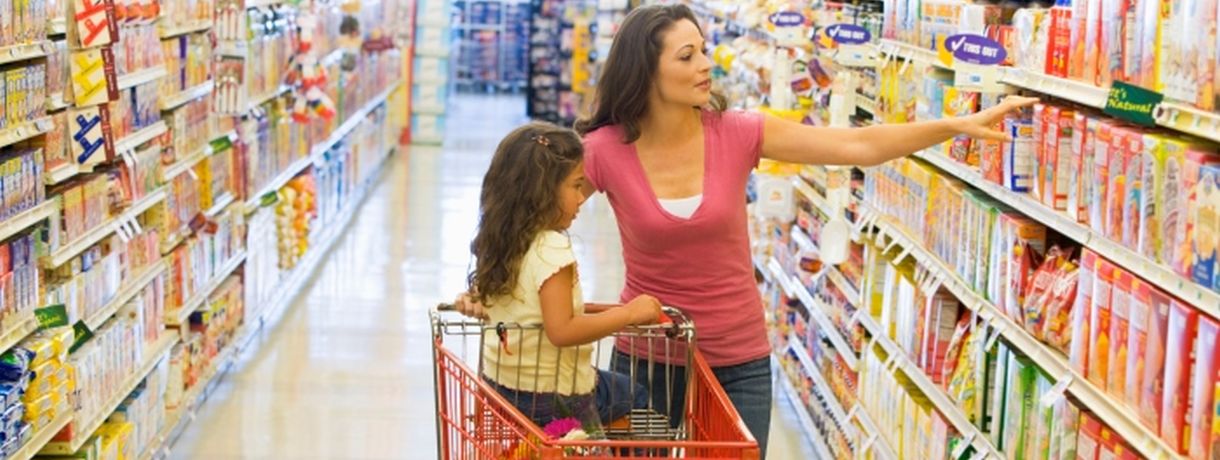 Mutter mit Kind im Einkaufswagen zwischen Supermarktregalen