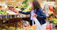 Junge Frau mit dunklen Locken und Winterjacke sucht Äpfel im Obstregal des Supermarktes