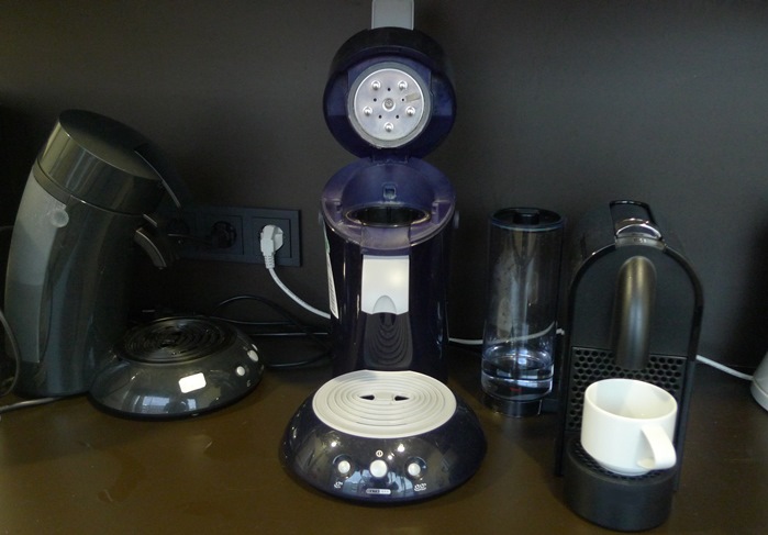 Wasserkocher und Kaffeemaschinen auf einer dunklen Arbeitsplatte mit Steckdosen.