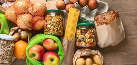 Diverse Lebensmittel wie Nudeln, Brot, Eier, Obst, Zwiebeln, usw. liegen auf einer braunen Unterlage