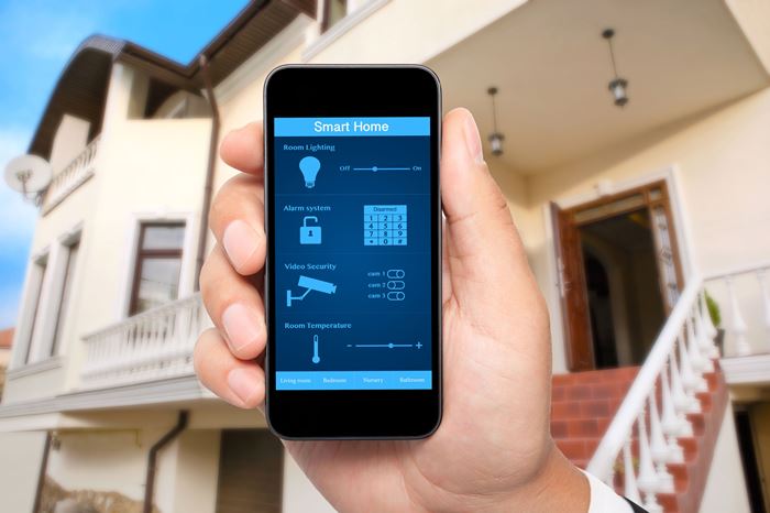 Eine Hand mit Smartphone mit Steuerelementen auf dem Display in Großaufnahme, dahinter ein Hauseingang Eine Hand mit Smartphone mit Steuerelementen auf dem Display in Großaufnahme, dahinter ein Hauseingang