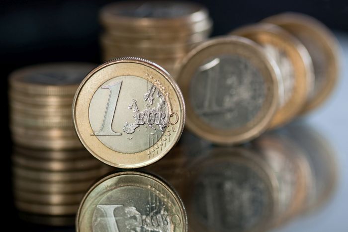 Mehrere Ein-Euro Münzen gestapelt und senkrecht stehend auf einer blank polierten, dunklen Oberfläche Mehrere Ein-Euro Münzen gestapelt und senkrecht stehend auf einer blank polierten, dunklen Oberfläche
