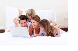 Familie mit Laptop Vierköpfige Familie mit weißem Laptop in weißem Bett. Papa hat eine Kreditkarte in der Hand
